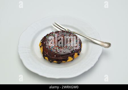 chocolate donut with sugar sprinkles on white plate with fork, close up. isolated on white background Stock Photo