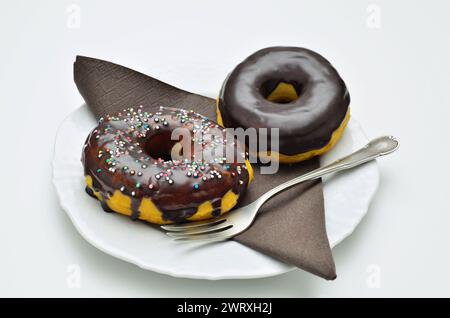 two chocolate donuts on white plate with fork and brown napkin, close up, isolated on white background Stock Photo