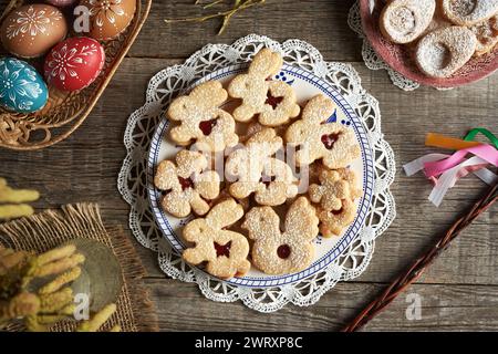 Homemade Linzer cookies in the shape of bunnies, chicken and four leaf clover, with Easter eggs in the background Stock Photo