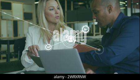 Image of connected icons over diverse coworkers discussing reports on laptop in office Stock Photo