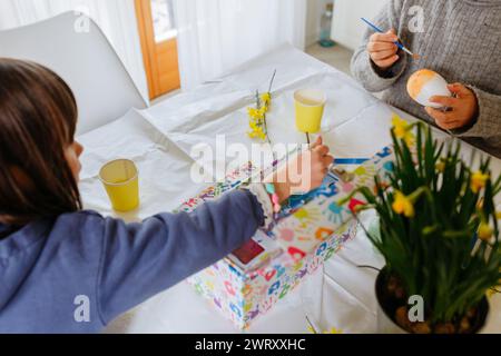 two children sitting at the kitchen table and decorating easter eggs Stock Photo