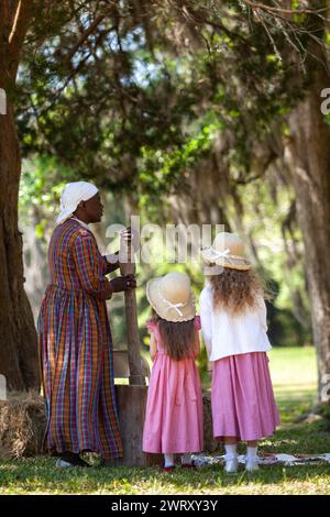 Sharon Cooper-Murray, a Gullah historic actor demonstrates how enslaved people threshed Carolina Gold rice to separate the grain from the chaff using a hand carved mortar as young children watch on the Charles Pinckney Snee Farm plantation at the Charles Pinckney National Historic Site in Mt Pleasant, South Carolina. Pinckney, a Founding Father of the United States, once owned 58 enslaved African-Americans at the plantation. Stock Photo
