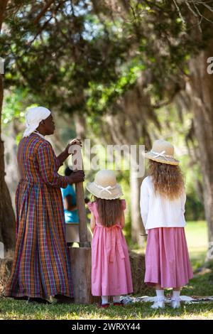 Sharon Cooper-Murray, a Gullah historic actor demonstrates how enslaved people threshed Carolina Gold rice to separate the grain from the chaff using a hand carved mortar as young children watch on the Charles Pinckney Snee Farm plantation at the Charles Pinckney National Historic Site in Mt Pleasant, South Carolina. Pinckney, a Founding Father of the United States, once owned 58 enslaved African-Americans at the plantation. Stock Photo