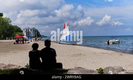 Silhouette of a couple sitting on the rocks next to the colorful beach scene at Lakeside Park Beach in Port Dalhousie, Ontario, Canada. Stock Photo