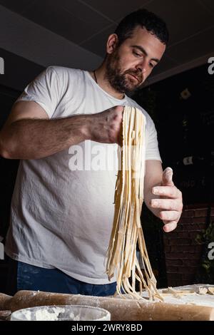 The chef delicately lifts the freshly made fettuccine after running the dough through the pasta machine. Vertical composition. Stock Photo