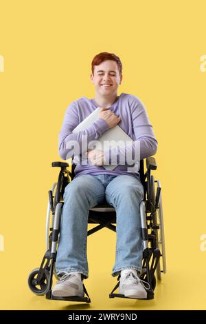 Young man in wheelchair with laptop on yellow background Stock Photo