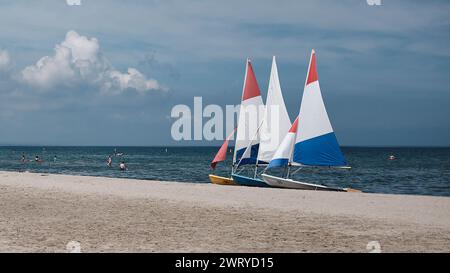 Three colorful small sailboats with red, white and blue sails pulled up on the beach on Lake Ontario, Canada.  Lakeside Park Beach, Port Dalhousie. Stock Photo