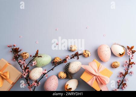 Easter flat lay with wrapped gifts, painted eggs, cherry blossoms and feathers on light blue background. Top view, copy space. Stock Photo