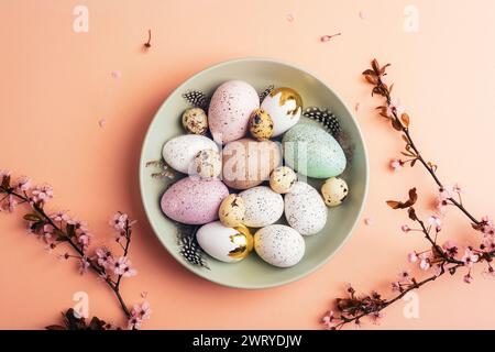 Easter eggs on green plate on light peach background with cherry blossom branches. Top view, flat lay. Stock Photo