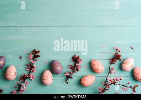 Easter flat lay with painted eggs, cherry blossoms and petals on turquoise blue background. Top view, copy space. Stock Photo