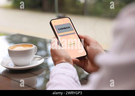 Cashback. Man holding smartphone at table indoors, closeup. Illustration of credit card and percent signs on device screen Stock Photo