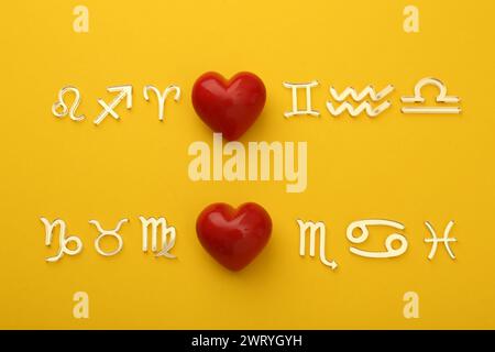 Zodiac compatibility. Signs with red hearts on yellow background, flat lay Stock Photo