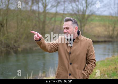 Middle aged man with gray hair and gray beard in a park in winter or spring pointing to side Stock Photo