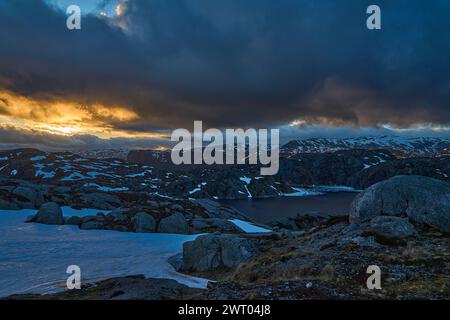dramatic sunset over an idyllic mountain lake with ice on the water and snow covered peaks in the background along the Lysebotn road on a sunny day in Stock Photo