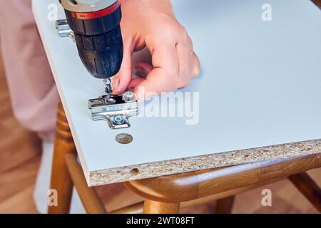 Furniture assembler installs adjustable door hinges into particle board of door cabinet from flat pack. Stock Photo