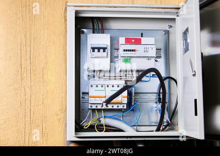 An open electrical panel is securely mounted on wooden wall, revealing an array of circuit breakers, wires, and safety switches. Stock Photo