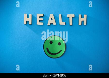 Generic health background with wooden cut out letters and green smiling emoticon isolated on blue background. Top view Stock Photo
