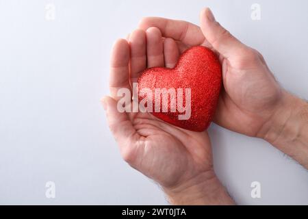 Two man's hands hugging a red glitter heart isolated on a white table. Top view. Stock Photo