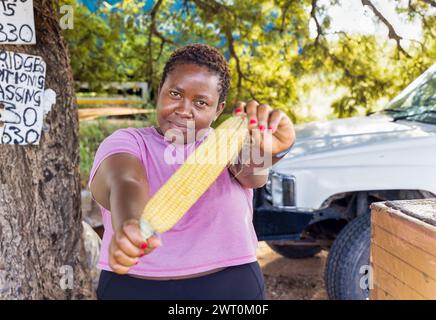 african woman street vendor selling corn on a street in the city on the sidewalk, car in the background Stock Photo