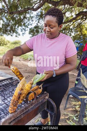 african woman street vendor selling corn on a street in the city on the sidewalk, car in the background Stock Photo