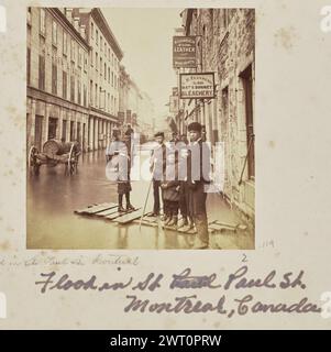 Flood in Saint Paul Street, Montreal. Alexander Henderson, photographer (Canadian, 1831 - 1913) 1869 A group of young and teenage boys stand on wooden planks on a flooded street. A number of men can be seen further behind them, as well as store signs outside of stone buildings that line the street. (Recto, mount) lower center, below image, in pencil: 'Flood in St. Paul St. Montreal [space] 2'; Lower center, below image, in purple ink: 'Flood in St [crossed out inscription] Paul St. / Montreal, Canada'; Stock Photo