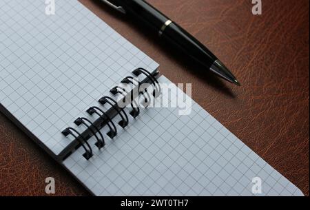 Classic Black Pen Near Spiral Notepad On Brown Leather Surface Stock Photo