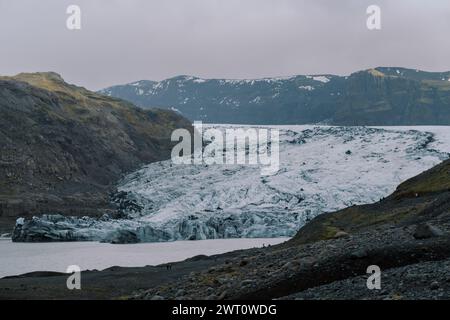 Cascade of glacial ice slides down contrast green grey mountainside Stock Photo