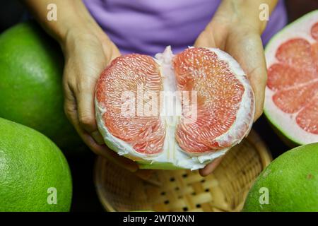 Cropped hand of woman holding Siam ruby pomelo fruit on table Stock Photo
