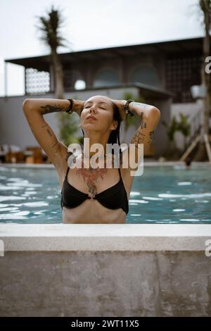 Young tattooed woman relaxing in the swimming pool. Stock Photo