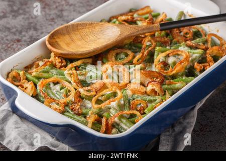 Delicious creamy Green Bean Casserole sprinkled with crispy fried onions on the baking dish on the table. Horizontal Stock Photo