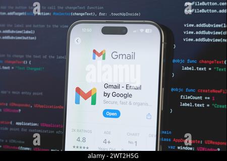 New York, USA - February 23, 2024: Gmail on iphone screen in blurred code programming background Stock Photo