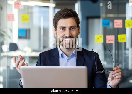 Confident businessman discussing project in modern office, surrounded by sticky notes and using a laptop. Stock Photo