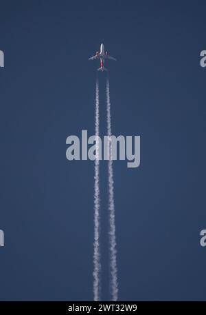 A commercial airliner at high altitude flies in a deep blue sky at sunset with contrails Stock Photo