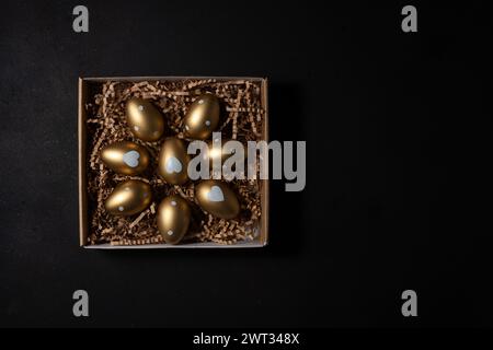 Gold eggs in paper box on black background. Top view. Stock Photo