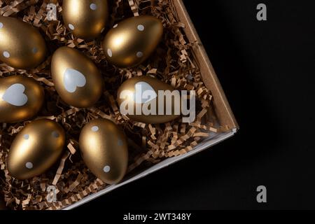 Gold eggs in paper box on black background. Stock Photo