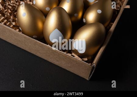 Golden eggs in paper box on dark table. Stock Photo
