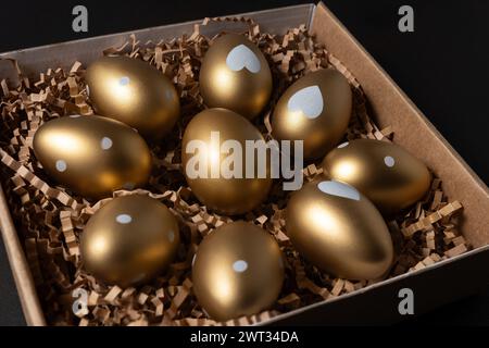 Golden eggs in paper box on dark table. Stock Photo