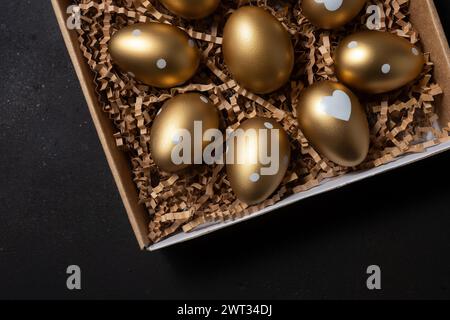 Golden eggs in paper box on dark table. Stock Photo
