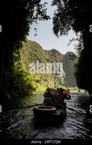 Small rowboats filled with tourists emerge from a cave on a river amid limestone mountains in Tam Coc, Ninh Binh province, northern Vietnam. Stock Photo