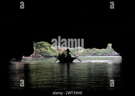 Silhouette of a small row boat carrying a group of tourists passing through a large, watery cave on a river in Tam Coc, Ninh Binh province, Vietnam. Stock Photo