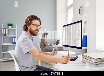 Serious man is focused on work with accounting program on computer and paper records. Stock Photo