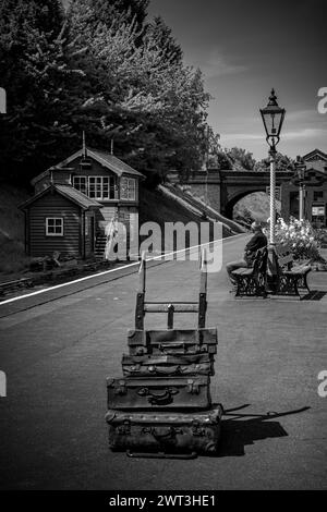 Vintage steam railway station platform with old luggage on barrow and one person waiting for train Stock Photo