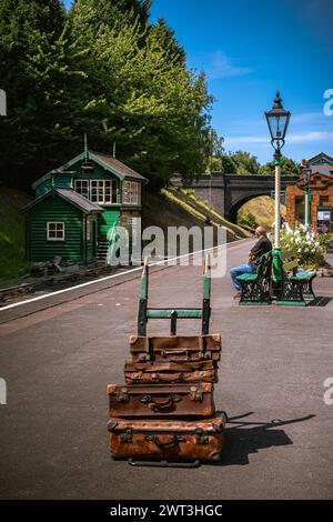 Vintage steam railway station platform with old luggage on barrow and one person waiting for train Stock Photo