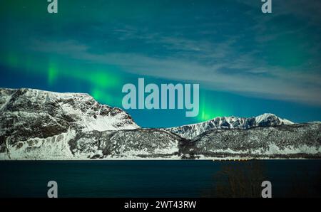 Majestic scenery of green northern lights over a fjord and snowy mountains on Hinnøya island in northern Norway. Stock Photo