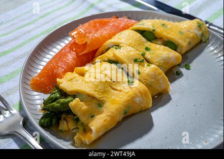 Chicken eggs omelette stuffed with green asparagus, served with smoked scottisch salmon fish, close up Stock Photo