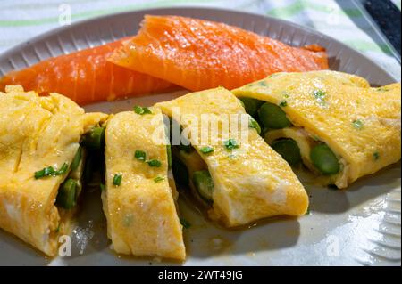 Chicken eggs omelette stuffed with green asparagus, served with smoked scottisch salmon fish, close up Stock Photo