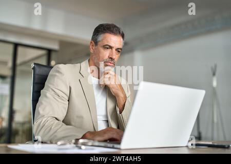 Busy mature professional business man looking at laptop working at office desk. Stock Photo