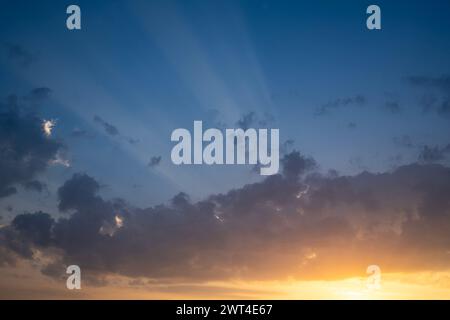 Sun rays passing through a cloud at sunset time, as the sky color turns from blue to golden. Stock Photo