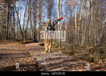 Cheerful woman with spread hands enjoys warm spring sunny day in city park on wooden trail Stock Photo