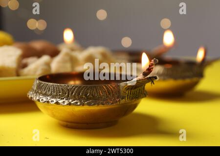 Happy Diwali. Diya lamp on yellow table against blurred lights, closeup Stock Photo